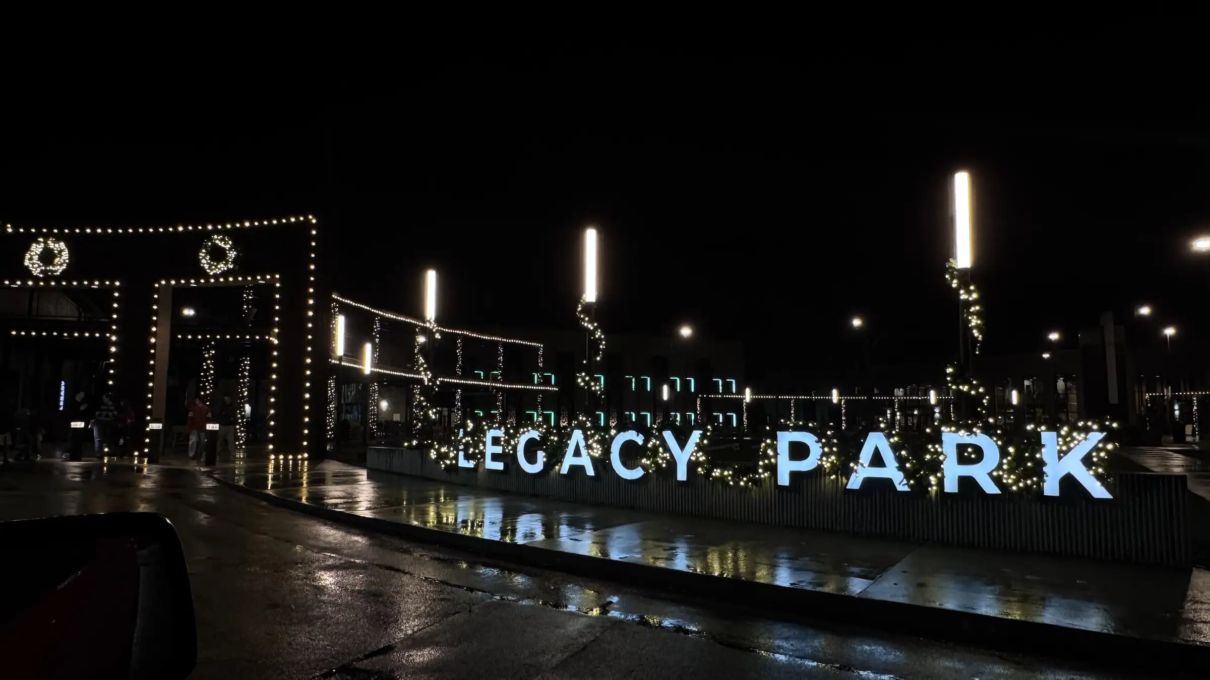 A commercial property entrance lit across its sign, arbors and walkways after dark