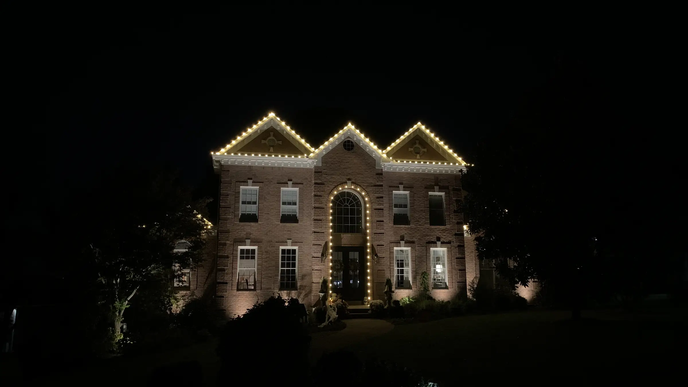 A large two story brick home in Goodlettsville, Tennessee with warm white lights along every roofline, gable and arched entry