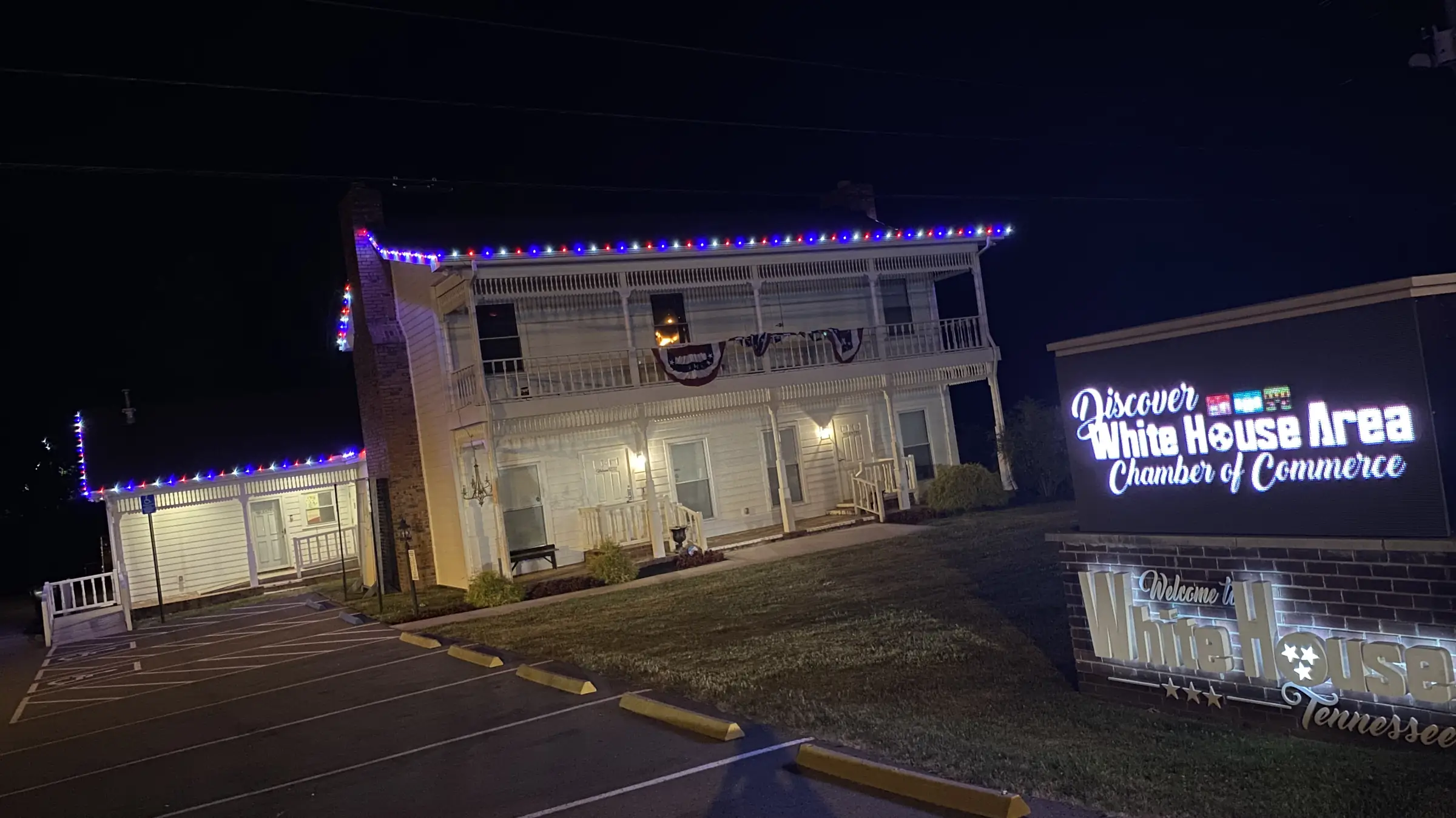 A civic building in White House, Tennessee lit along its roofline beside an illuminated town welcome sign