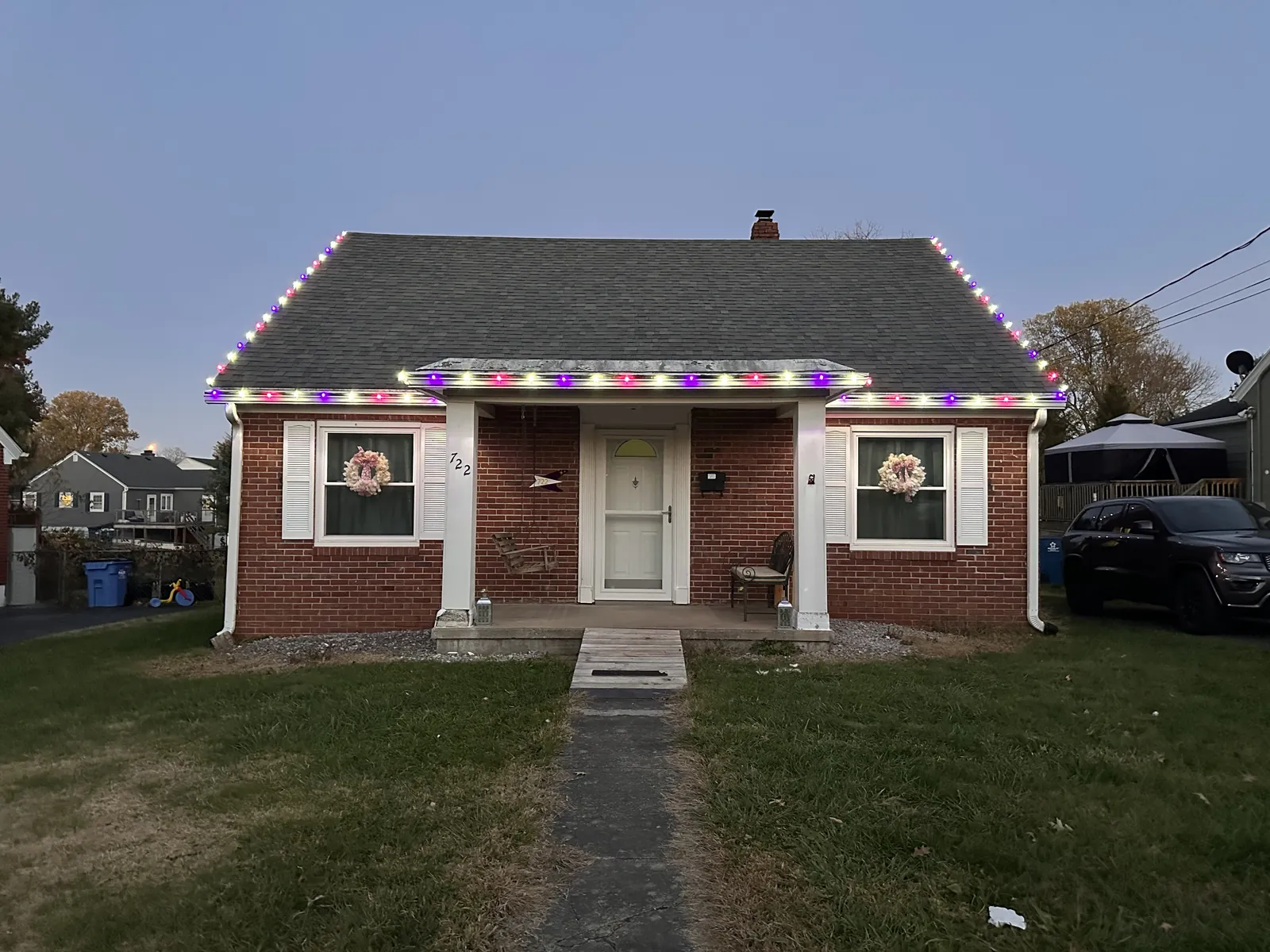 A brick cottage with multicolor lights along the roofline and lit wreaths in the front windows
