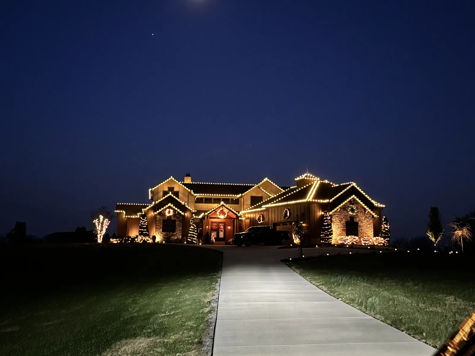 A wide home at the end of a lit driveway, warm white on every roofline and peak