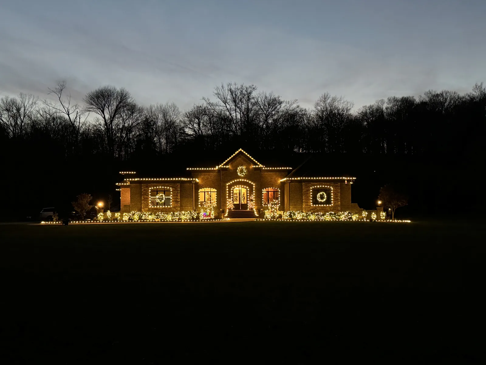 A house lit warm white across its full frontage and both wings, seen from across a dark lawn