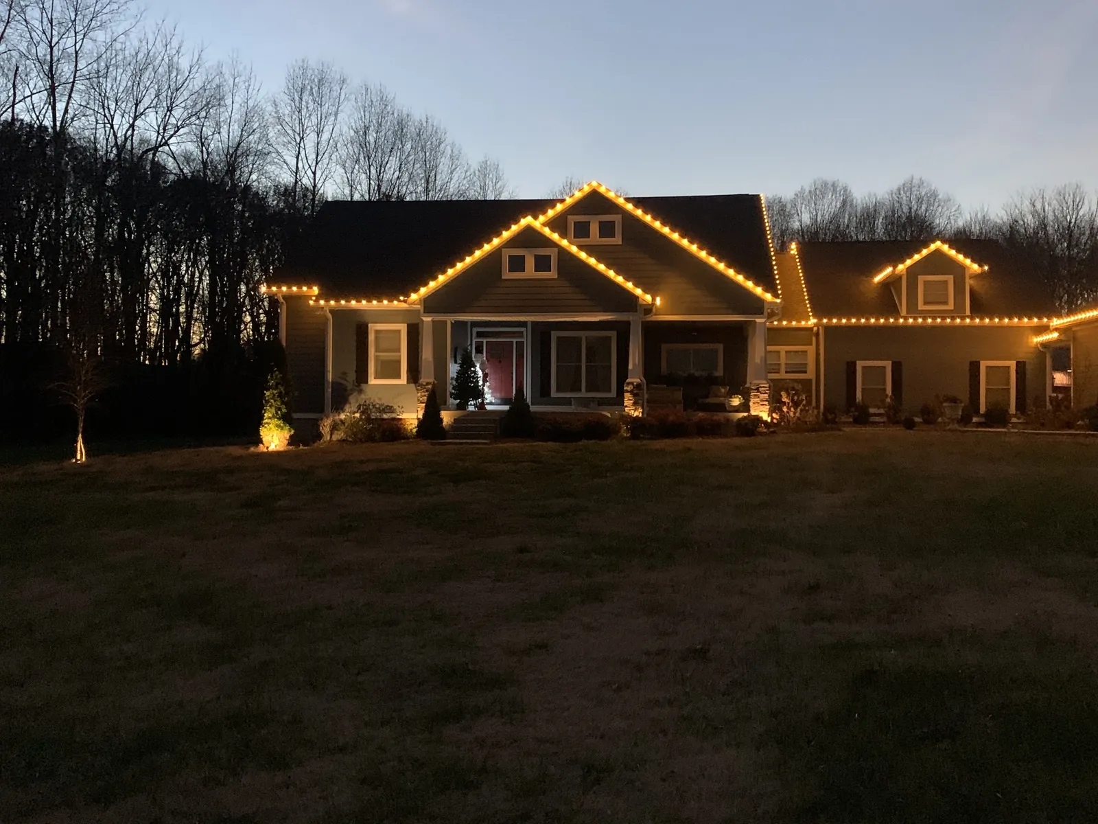 A long single story home with warm white lights following the roofline and porch against a deep blue dusk sky