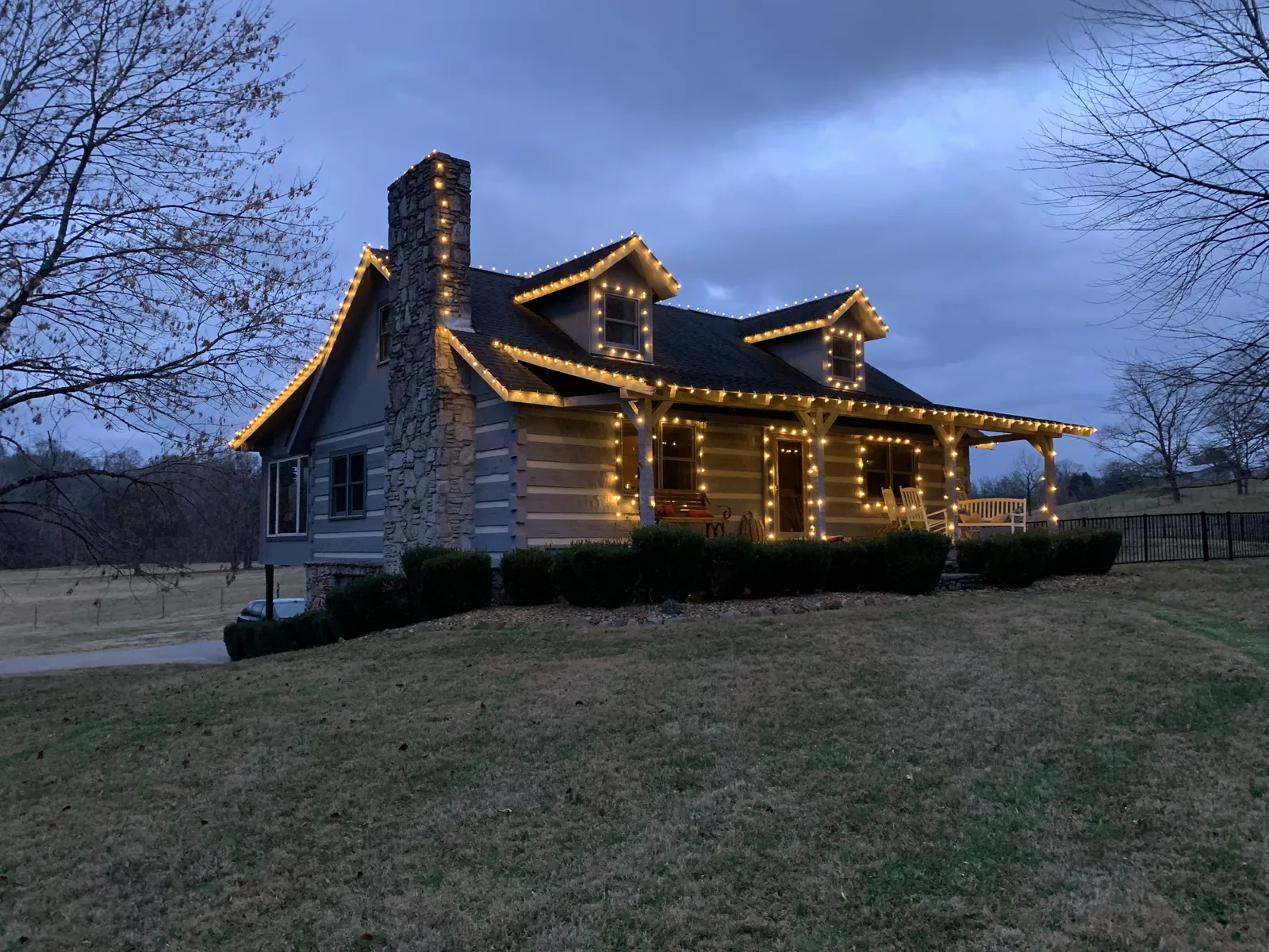A log home in White House, Tennessee at dusk, warm white lights along every roofline and gable