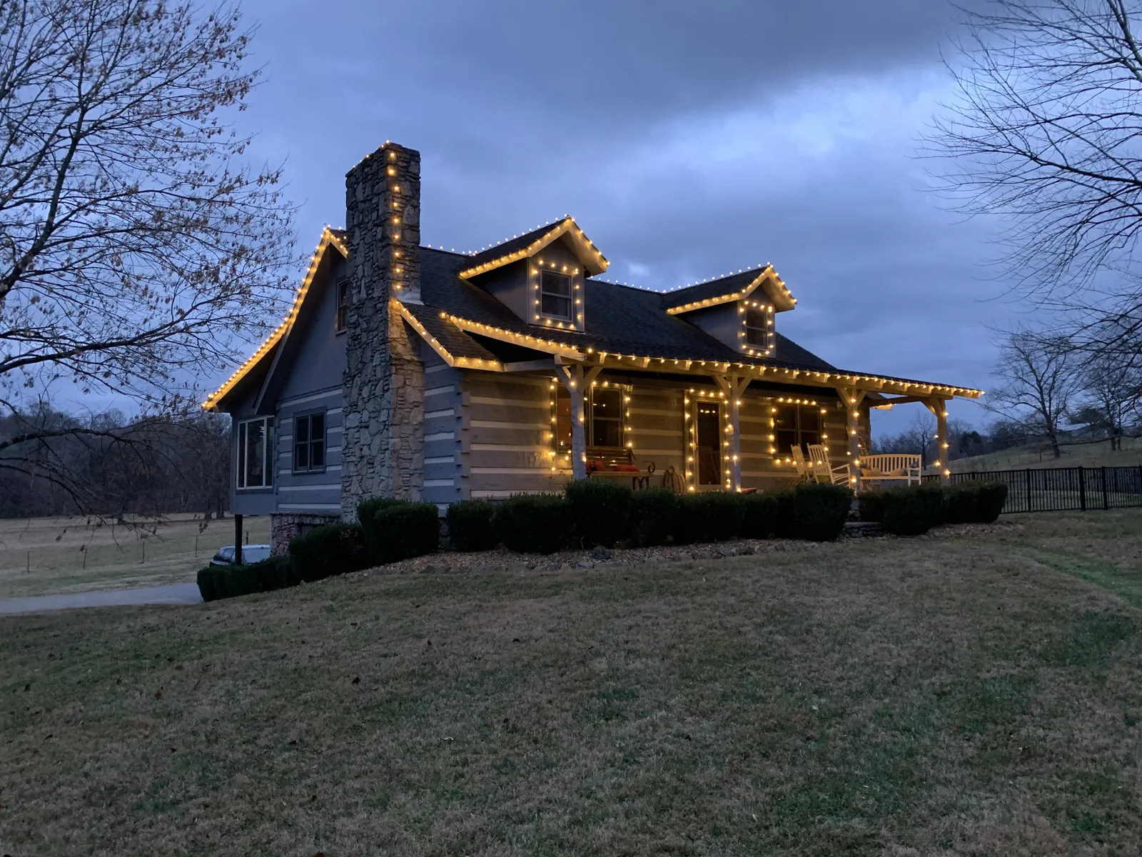 A log home in White House, Tennessee at dusk, warm white lights along every roofline and gable