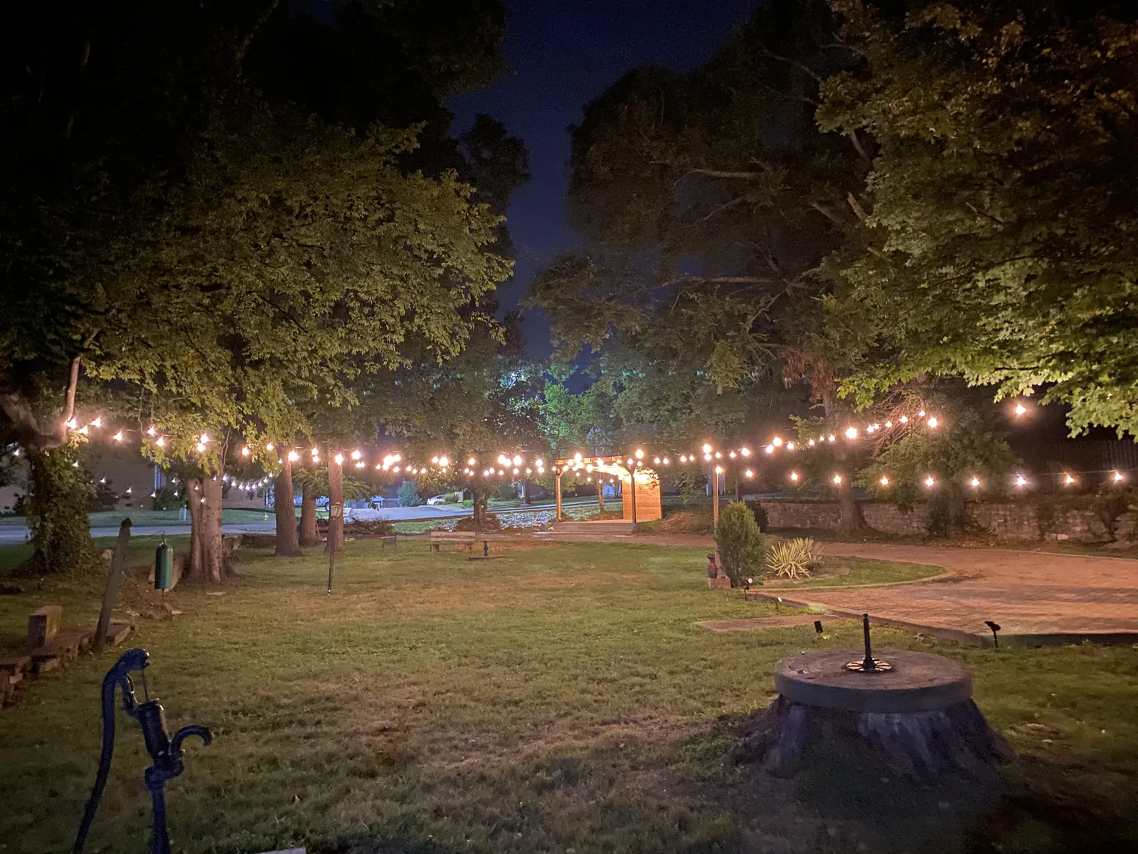Strands of string lights running between mature trees over a lawn and a brick path at night in Gallatin, Tennessee
