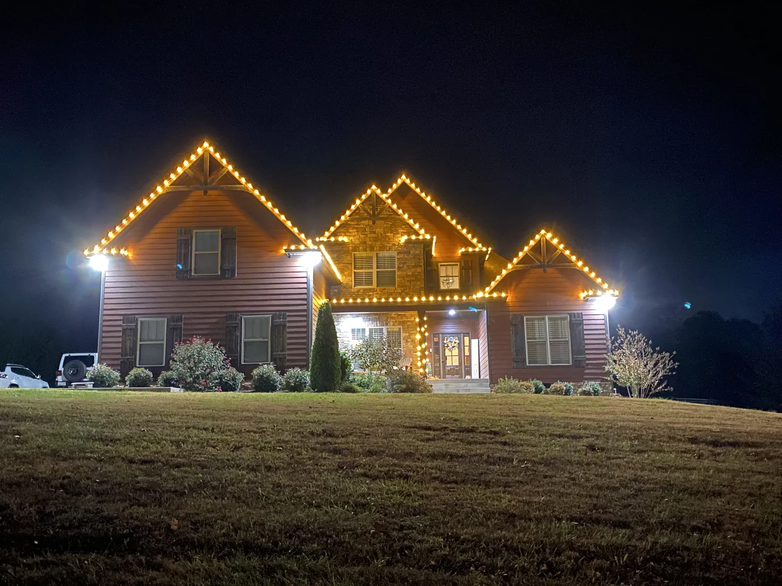 A two story home with warm white lights tracing the roofline, gables and garage