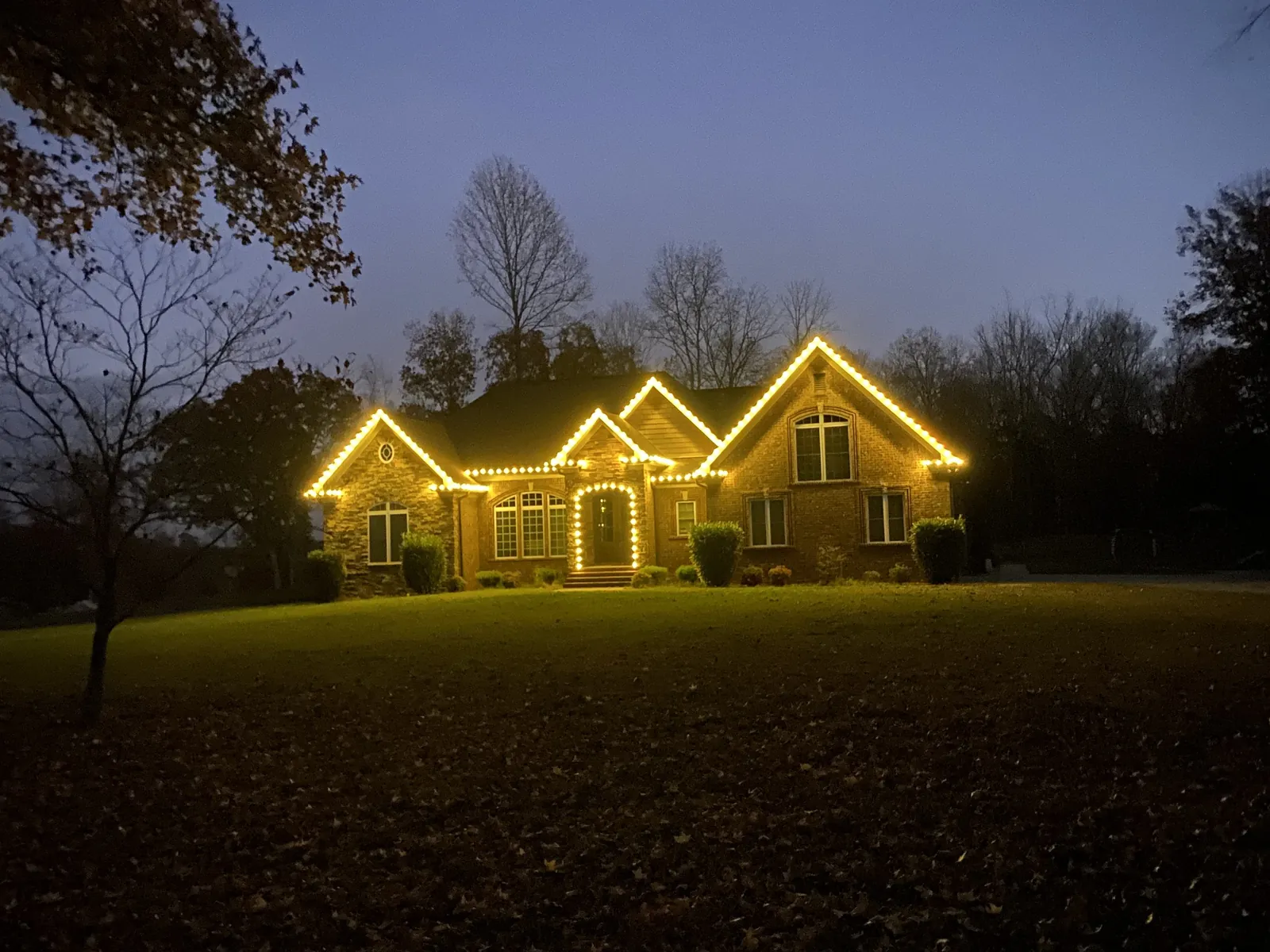 A house lit warm white along every roofline and gable, glowing across a wide dark lawn