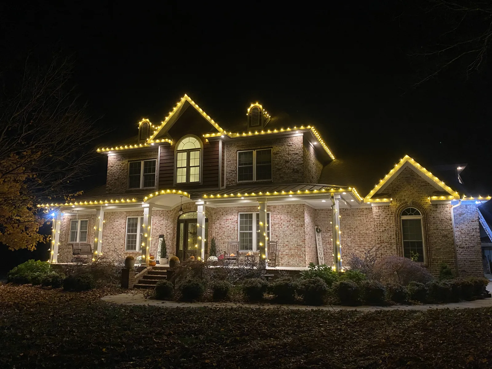 A two story home with warm white lights following the roofline, gables and dormers against a dark sky