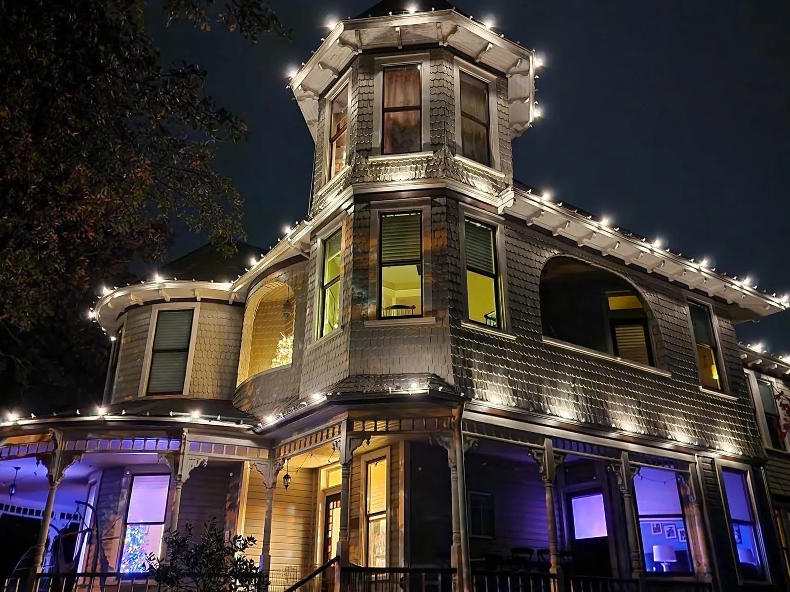 The Victorian house in warm white and amber, the turret and porch picked out against a black sky